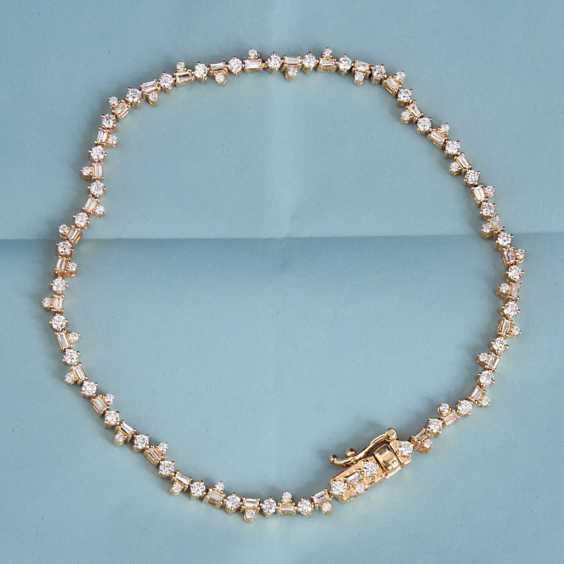 A coiled tennis necklace with bright pink gemstones set in gold, arranged in a circular shape on a white background