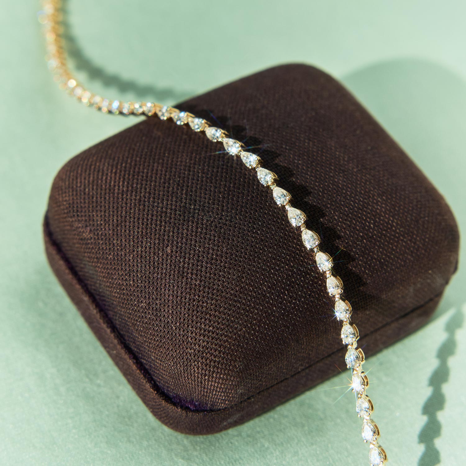 A coiled tennis necklace with bright pink gemstones set in gold, arranged in a circular shape on a white background