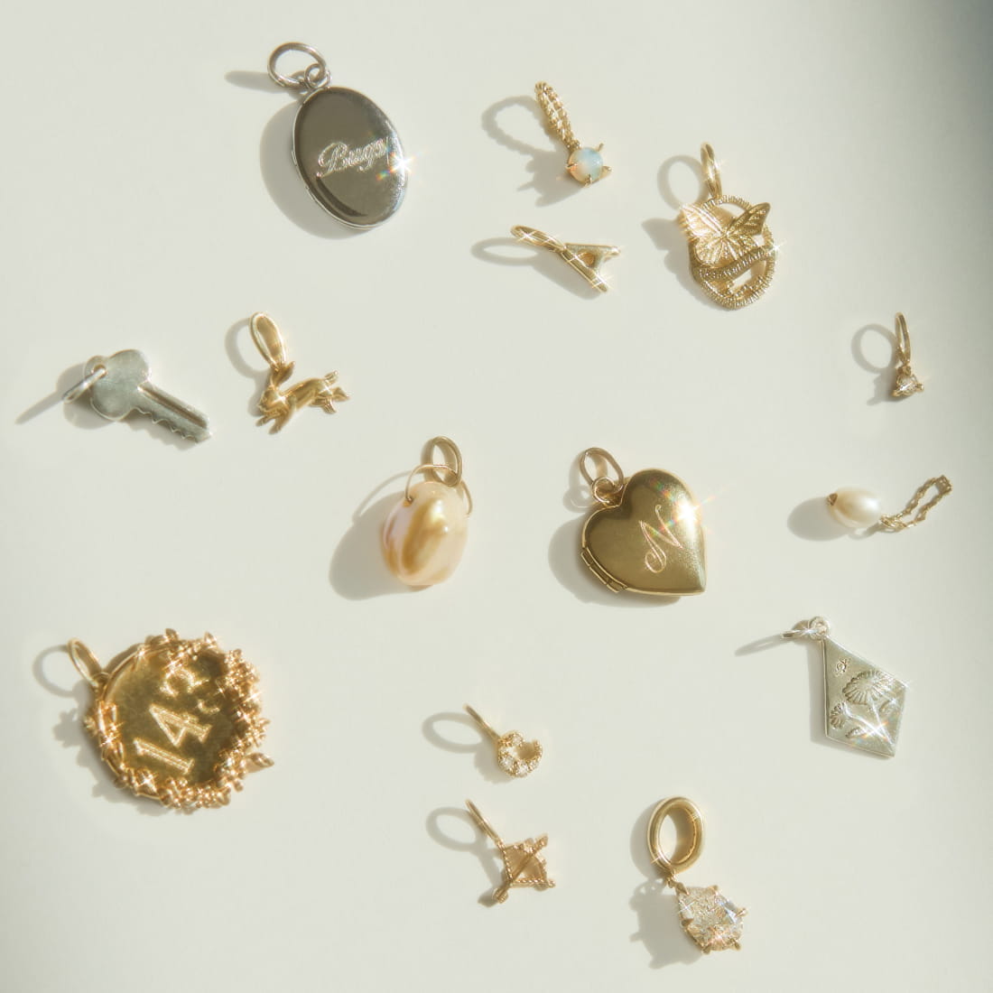 A wrist adorned with two delicate gold chain bracelets, each with small charms, two zodiac charms and one alphabet charm.