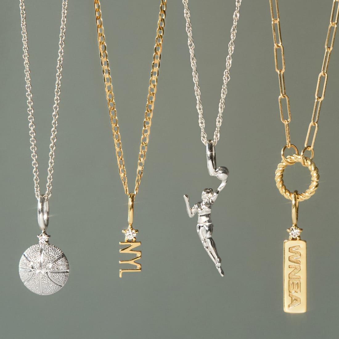 A collection of four necklaces, including a silver basketball charm, a gold "NYL" pendant, a silver figurine of a female athlete, and a gold "WNBA" tag, displayed against a gray background.