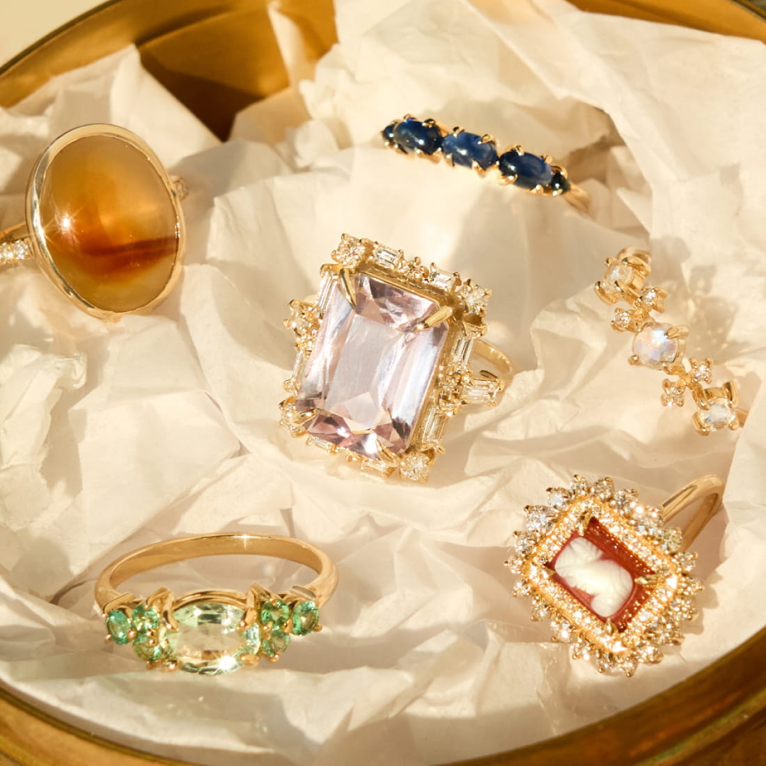 A close-up of a hand with three colorful rings and a silver necklace featuring an iridescent pendant.