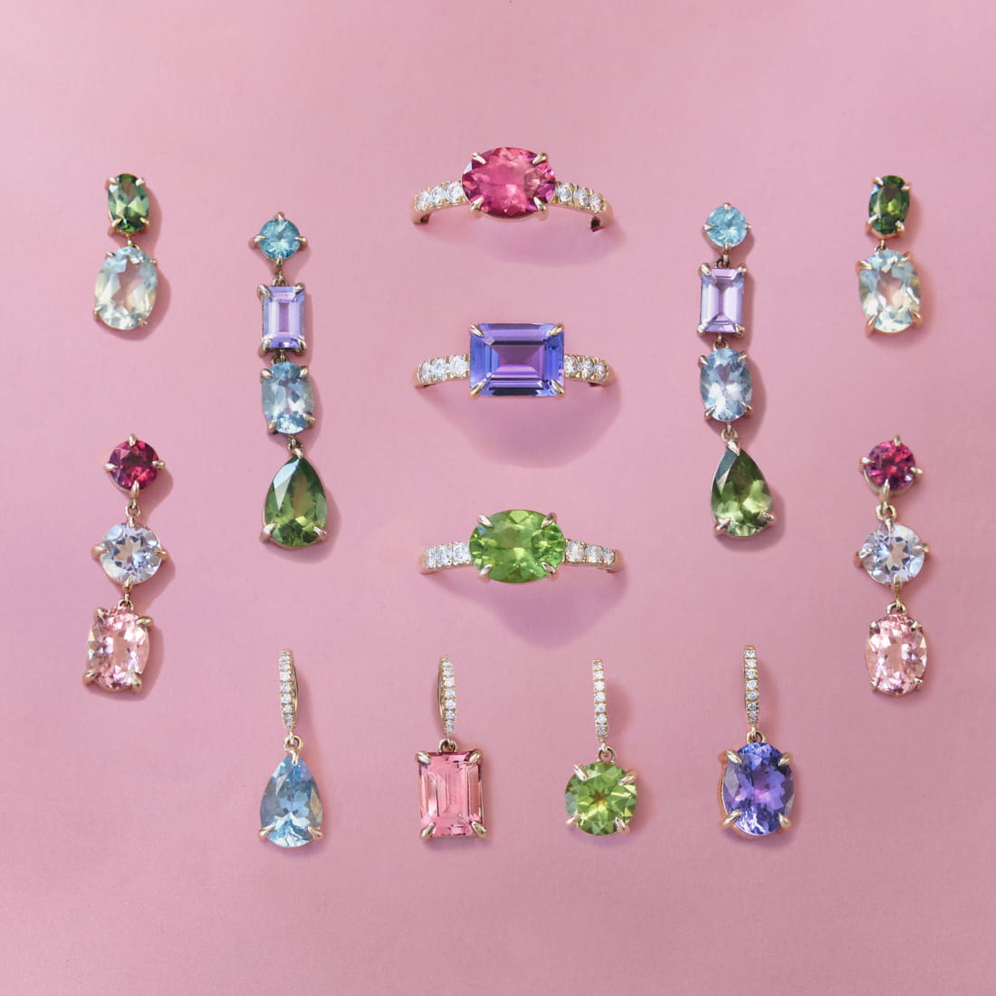An assortment of colorful jewelry pieces, including rings and earrings, displayed on a pink background. The rings feature pink, purple, and green gemstones, while the earrings showcase various stones in blue, green, and pink.