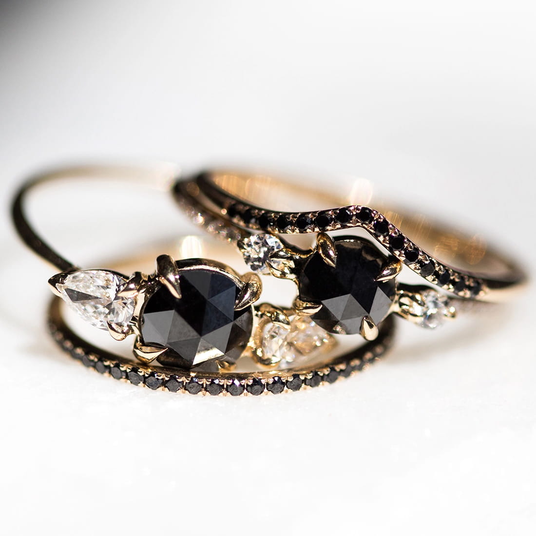 Two intertwined gold rings with black heart-shaped gemstones, clear accent diamonds, and dark-stone bands.