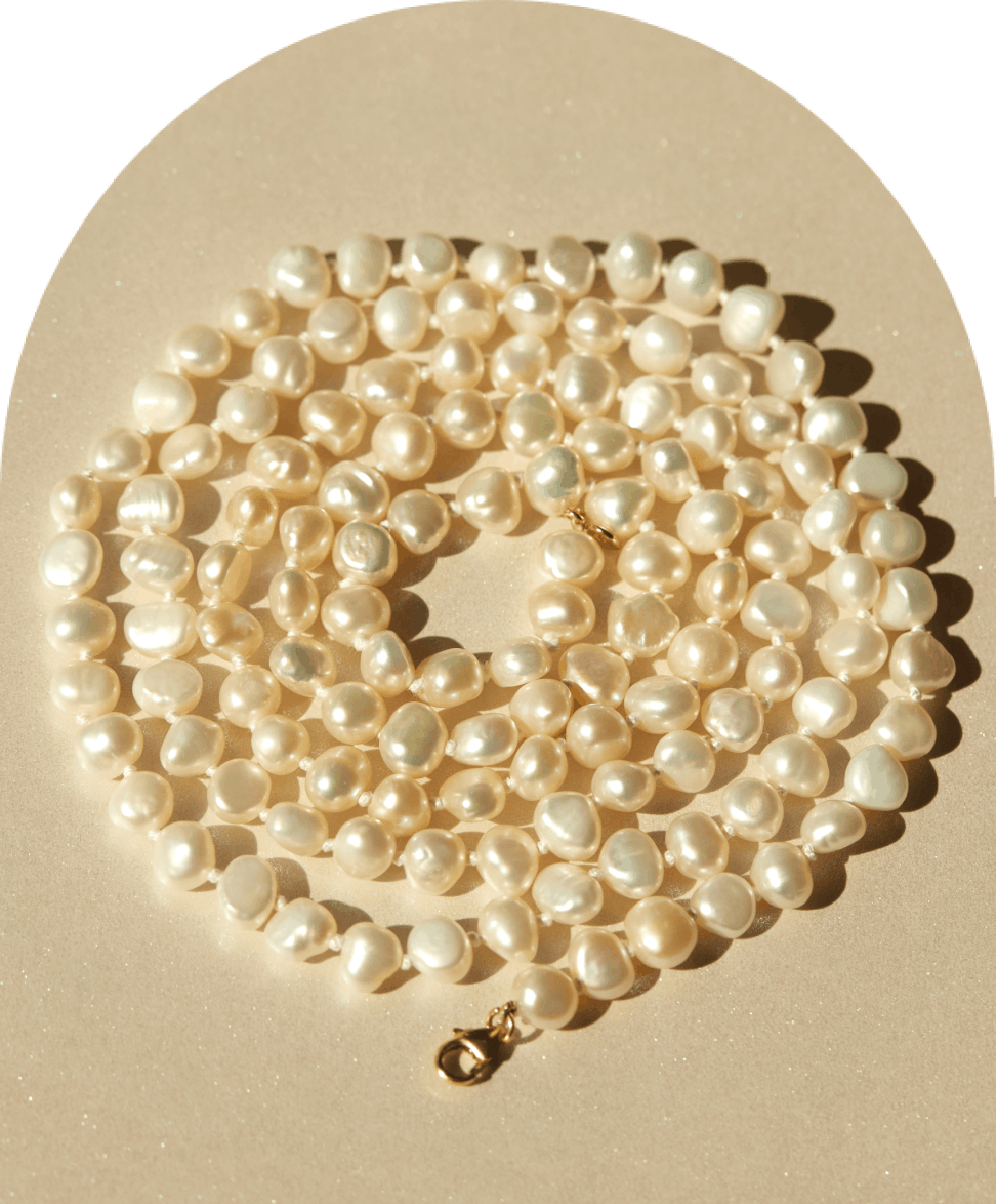 A string of irregularly shaped, lustrous white pearls laid out in a spiral on a shimmering beige surface.