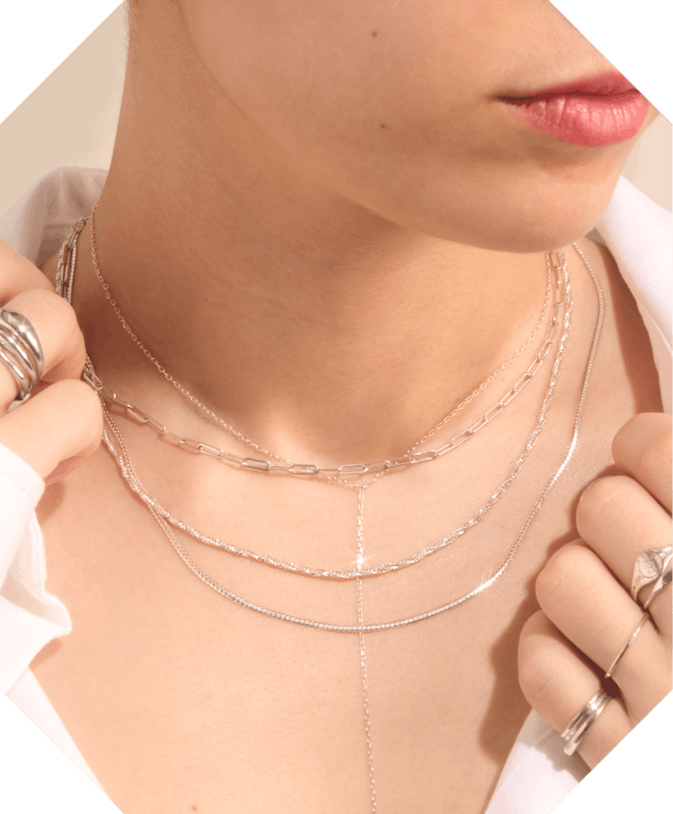 A person wearing layered silver necklaces and rings, dressed in a white shirt.