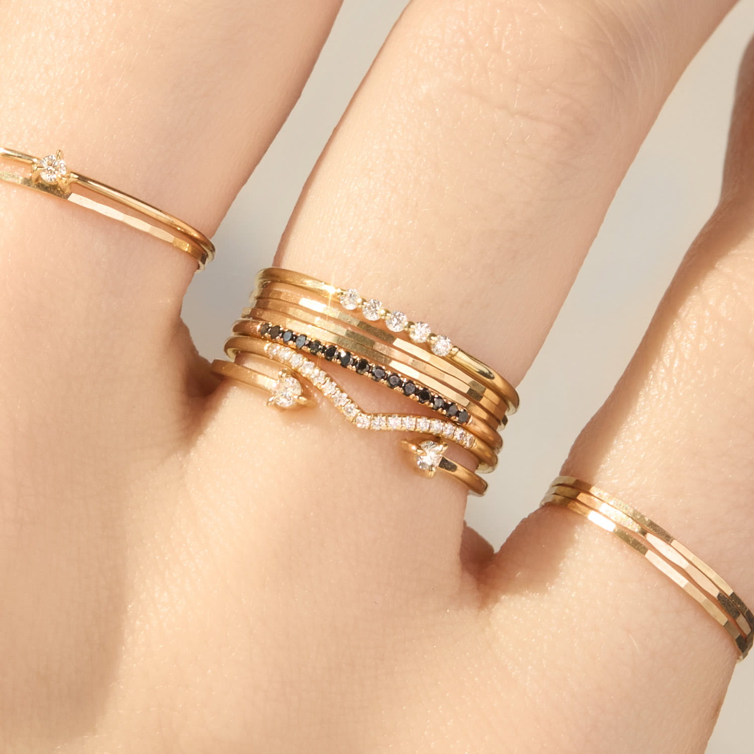 Close up of a person's fingers with two threadbare rings stacked on the left, pointelle diamond ring stacked on the grand coupe ring and on the right twisted stacker stacked on grand painter's ring
