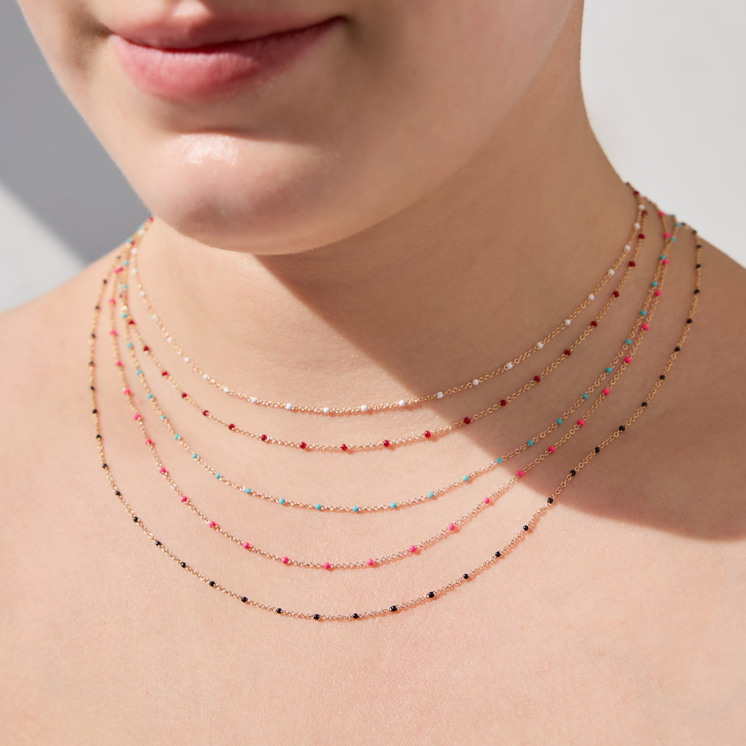 A close-up of a person's neck featuring multiple layered necklaces with colorful beads in red, blue, pink, and black.